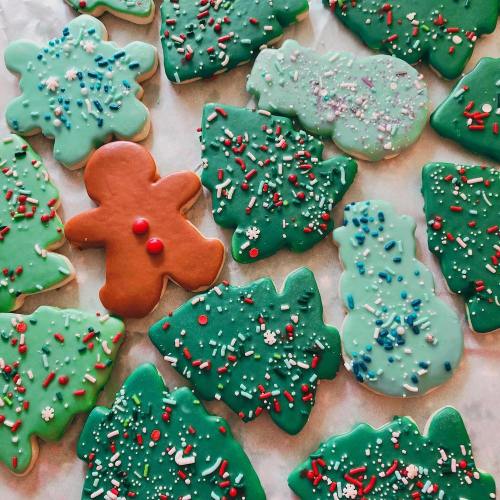 A variety of decorated Christmas cookies, including green trees, a gingerbread man, and snowmen, all with colorful sprinkles.