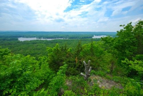 A scenic view of a lush green landscape with a river winding through it, under a partly cloudy sky.
