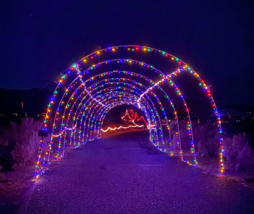 A colorful archway of lights illuminates a dark pathway, creating a festive atmosphere at night.