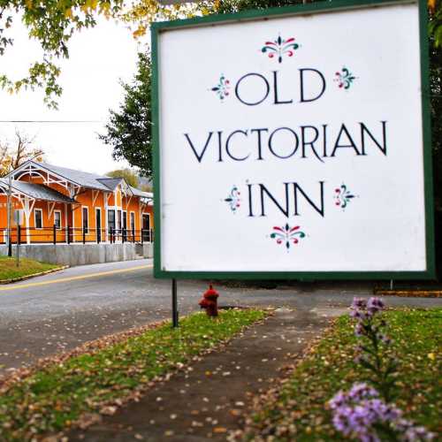 Sign for "Old Victorian Inn" with a colorful building and greenery in the background.