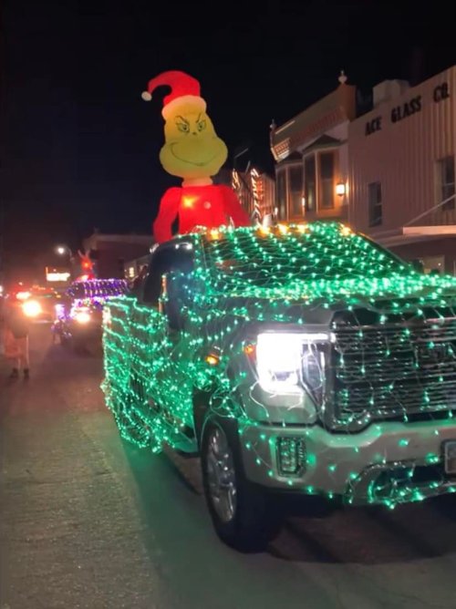 A truck decorated with green lights and a large Grinch figure on top, driving in a festive night parade.