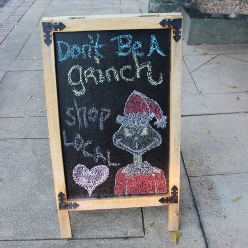 Chalkboard sign featuring a Grinch in a Santa hat with the text "Don't be a Grinch, shop local!" and a heart.