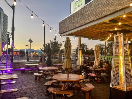 Outdoor seating area with wooden tables, umbrellas, and string lights, set against a sunset backdrop.