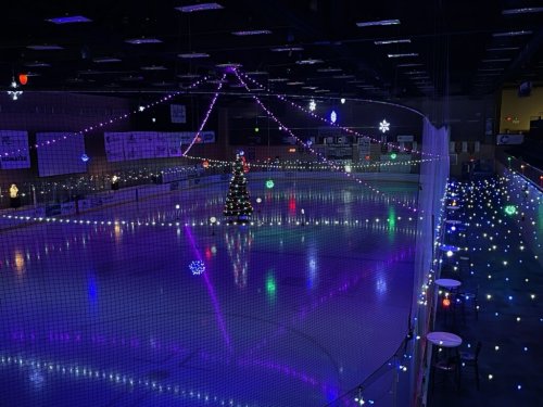 An ice rink decorated with colorful lights and a Christmas tree, creating a festive atmosphere.