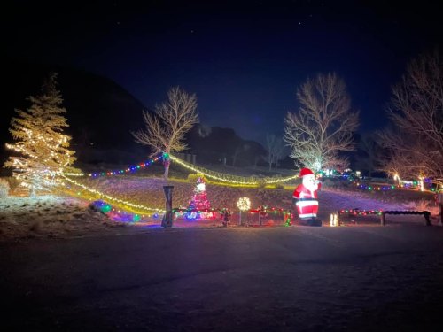 A festive outdoor scene at night with colorful Christmas lights, a decorated tree, and a large Santa figure.