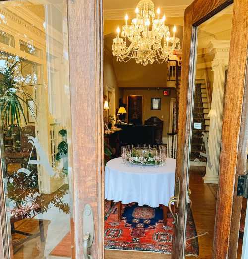 View through a wooden door into a warmly lit foyer with a chandelier, table, and elegant decor.