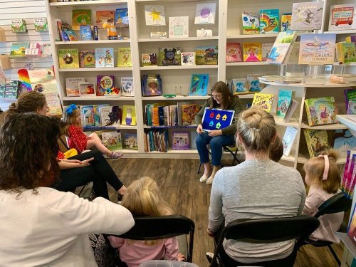 A storyteller shares a book with children seated in a cozy bookstore, surrounded by colorful children's books.