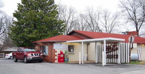 A small barbecue restaurant with a red roof, outdoor menu, and a red pickup truck parked outside. Trees in the background.