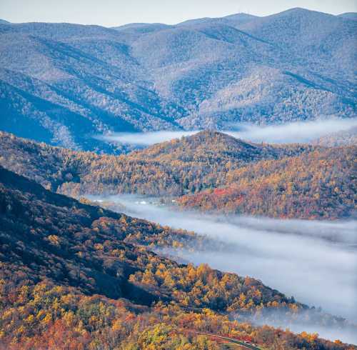 A scenic view of mountains with autumn foliage and mist in the valleys, showcasing vibrant colors and rolling hills.