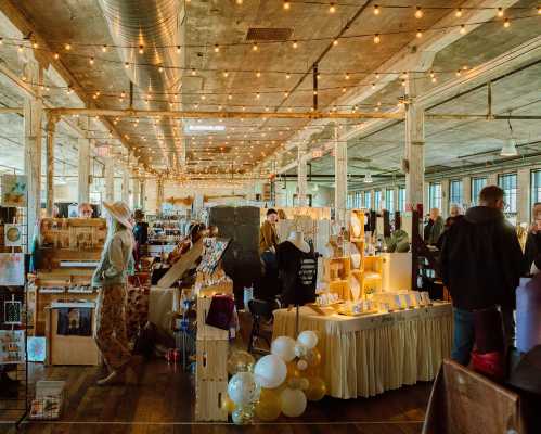 A bustling market scene with vendors and shoppers, string lights overhead, showcasing various handmade goods.