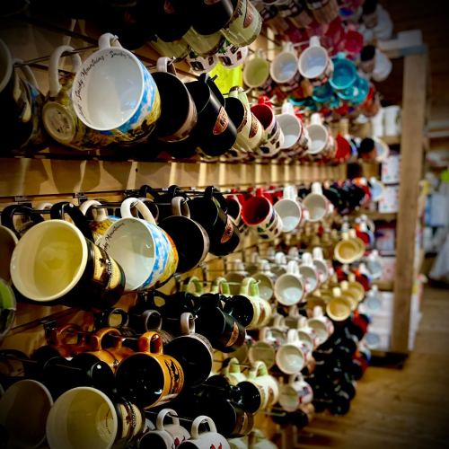 A colorful display of various mugs hanging on a wooden wall, showcasing different designs and colors.
