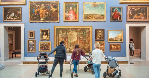Visitors with strollers admire various paintings in a gallery, surrounded by ornate frames and colorful artworks.