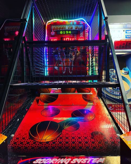 A brightly lit basketball arcade game with a scoring system and several basketballs on the floor.