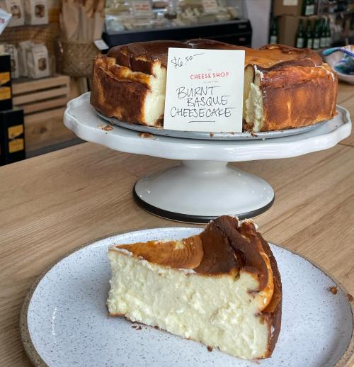 A slice of burnt basque cheesecake on a plate next to a whole cheesecake on a stand, with a price tag of $6.50.