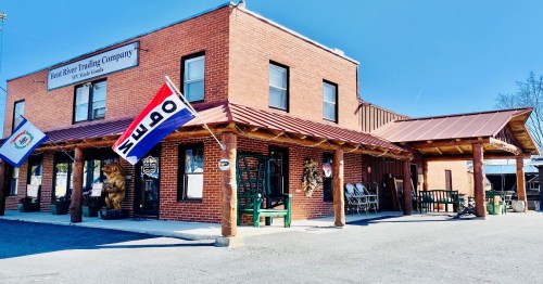 A brick building with a metal roof, featuring flags and signage for the Red River Trading Company in a sunny setting.