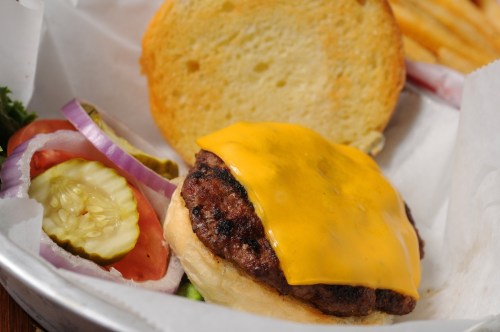 A cheeseburger with melted cheddar, lettuce, tomato, pickles, and onion, served with a side of fries.