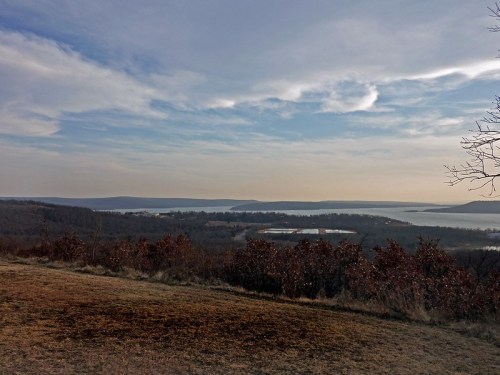 A scenic view of a lake surrounded by hills and trees under a cloudy sky.