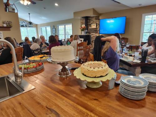 A cozy gathering with people chatting around a table, featuring cakes and a variety of food in a warm, inviting space.