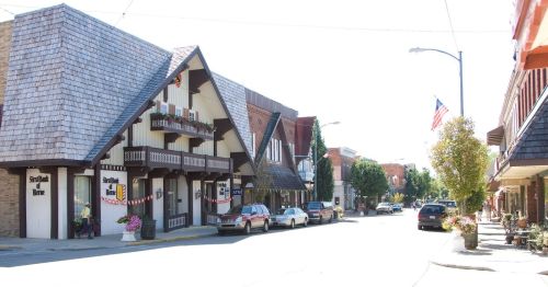 A charming street scene featuring quaint buildings, parked cars, and decorative planters under a clear blue sky.