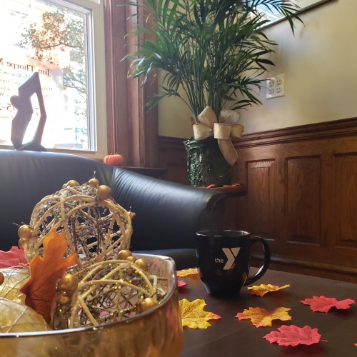 A cozy indoor scene with a plant, a black mug, and decorative autumn leaves on a table.