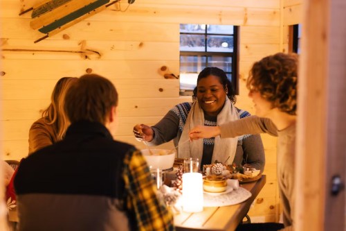A group of friends enjoying a meal together in a cozy wooden cabin, sharing food and laughter.