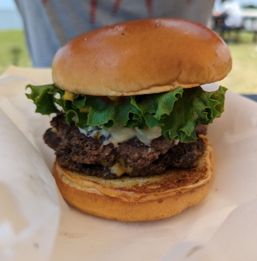 A close-up of a juicy burger with lettuce and sauce on a toasted bun, resting on a white wrapper.