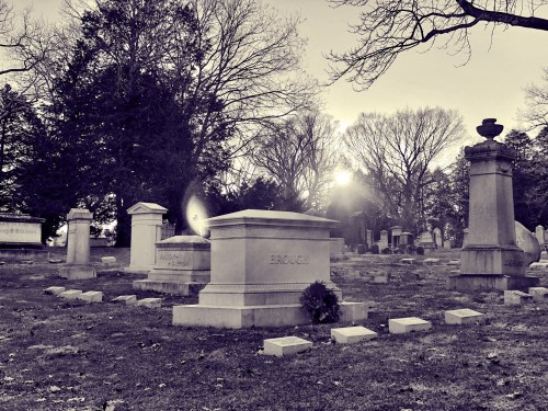 A serene cemetery scene at sunset, featuring gravestones and trees, with a wreath placed on one of the graves.