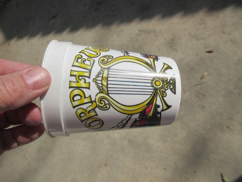 A hand holding a white cup featuring colorful illustrations and the word "Orpheus."