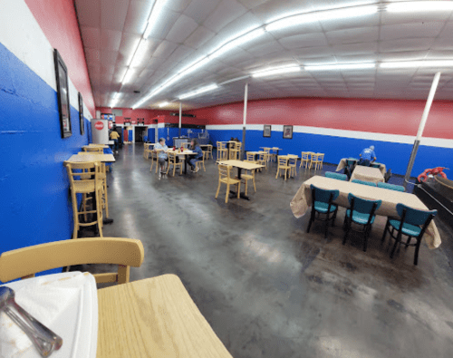 A spacious restaurant interior with blue and red walls, empty tables, and chairs arranged for dining.