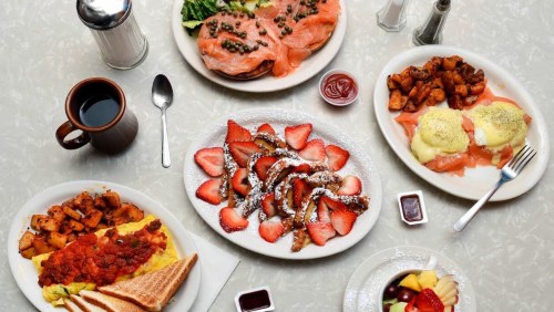 A table spread with breakfast dishes: smoked salmon, eggs Benedict, French toast with strawberries, potatoes, and coffee.