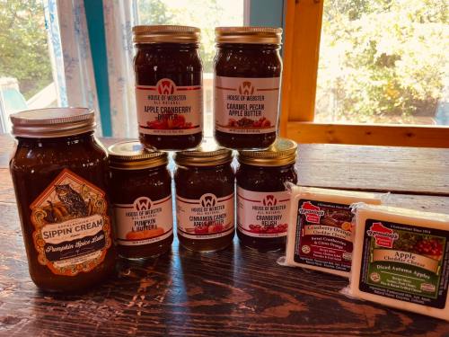 A collection of jars featuring various fruit butters and spreads, alongside a jar of pumpkin spice and cheese blocks.