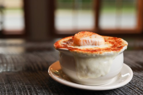 A bowl of French onion soup topped with melted cheese and a toasted bread slice, served on a small plate.