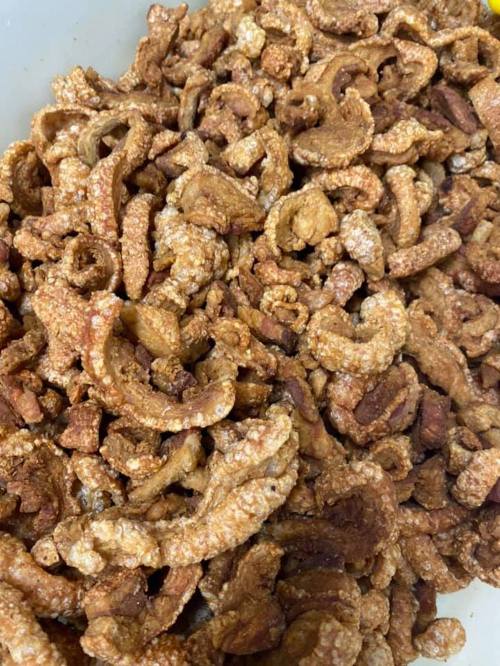 A close-up of crispy, golden-brown pork cracklings piled together in a bowl.