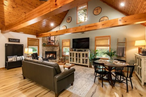 Cozy living room with wooden beams, a fireplace, a TV, and comfortable seating, featuring warm lighting and decor.