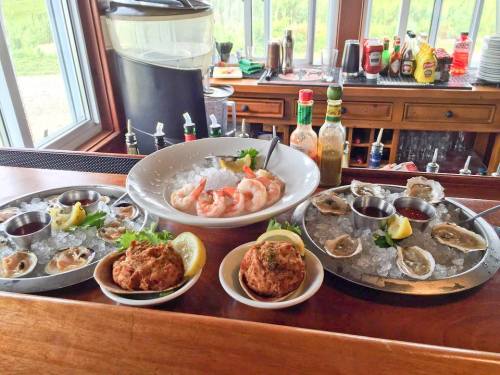 A seafood platter featuring shrimp, oysters, and crab cakes on ice, with sauces and garnishes, displayed at a bar.