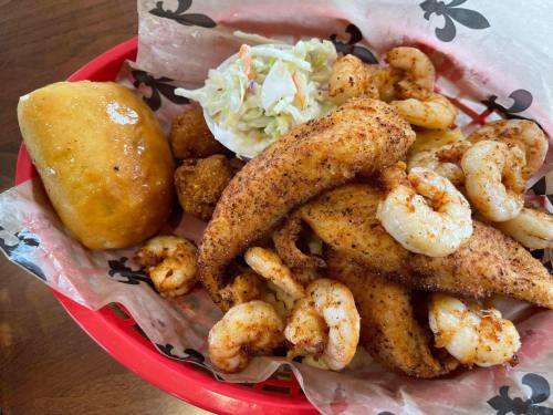 A red basket filled with seasoned fried fish, shrimp, coleslaw, hushpuppies, and a soft roll.