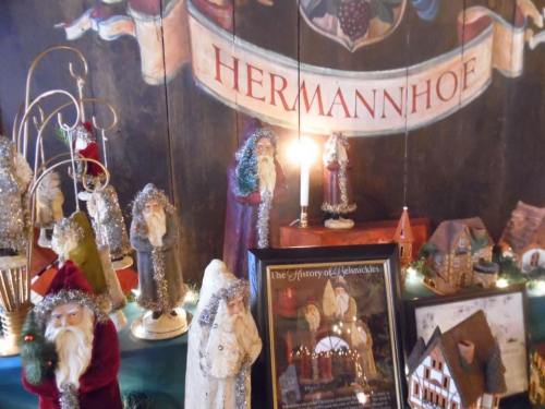 A festive display featuring decorative figures, candles, and a sign reading "Hermannhoe" against a wooden backdrop.