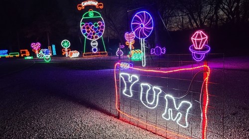 Colorful holiday lights display featuring candy-themed decorations and a sign that reads "YUM."