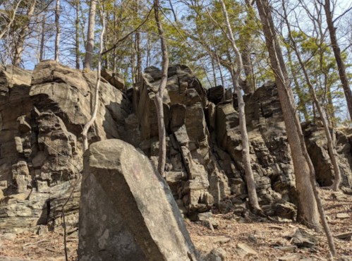 Rocky cliffside with large boulders and sparse trees under a clear blue sky.