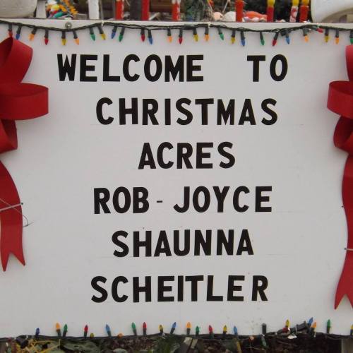 Sign welcoming visitors to Christmas Acres, featuring names Rob, Joyce, Shaunna, and Scheitler. Decorated with bows and lights.