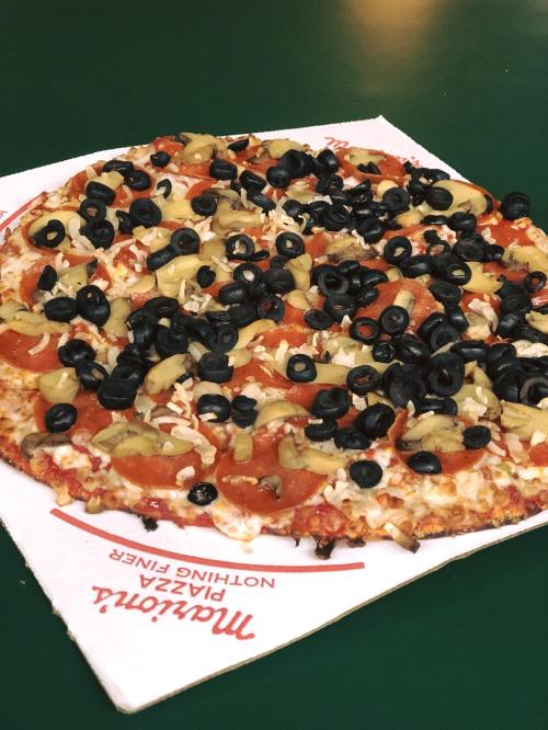 A pizza topped with pepperoni, black olives, green olives, and shredded cheese on a white paper plate.