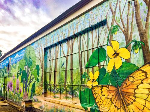 Colorful mural depicting a forest scene with trees, flowers, and a butterfly on a building wall.