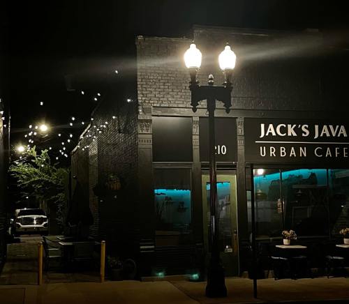 A cozy urban café at night, with string lights and a vintage streetlamp illuminating the entrance.