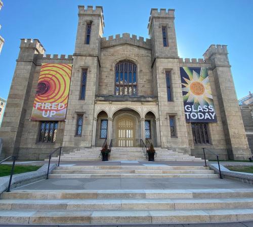 Historic stone building with castle-like architecture, featuring banners that read "FIRED UP" and "GLASS TODAY."