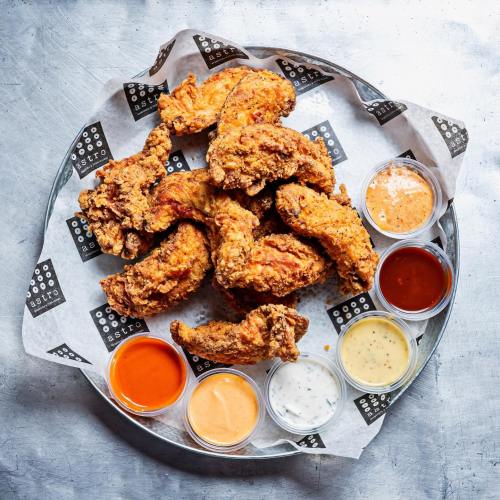 A platter of crispy fried chicken wings surrounded by various dipping sauces on a paper-lined tray.