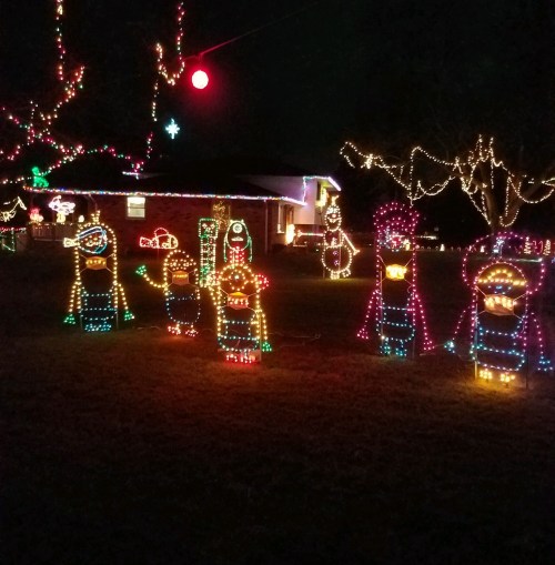 Colorful holiday lights illuminate snowman figures in a festive yard at night, creating a cheerful winter scene.