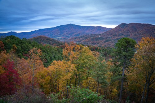 A scenic view of mountains and colorful autumn foliage under a cloudy sky.