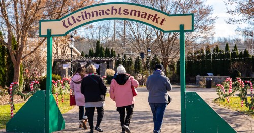 Four people walk under a sign reading "Weihnachtsmarkt," surrounded by festive decorations in a winter setting.