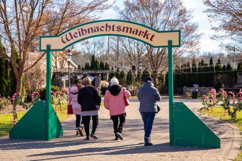 People walking under a festive archway labeled "Weihnachtsmarkt," surrounded by holiday decorations and trees.