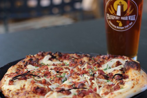 A close-up of a pizza topped with cheese, meat, and herbs, alongside a glass of amber beer.